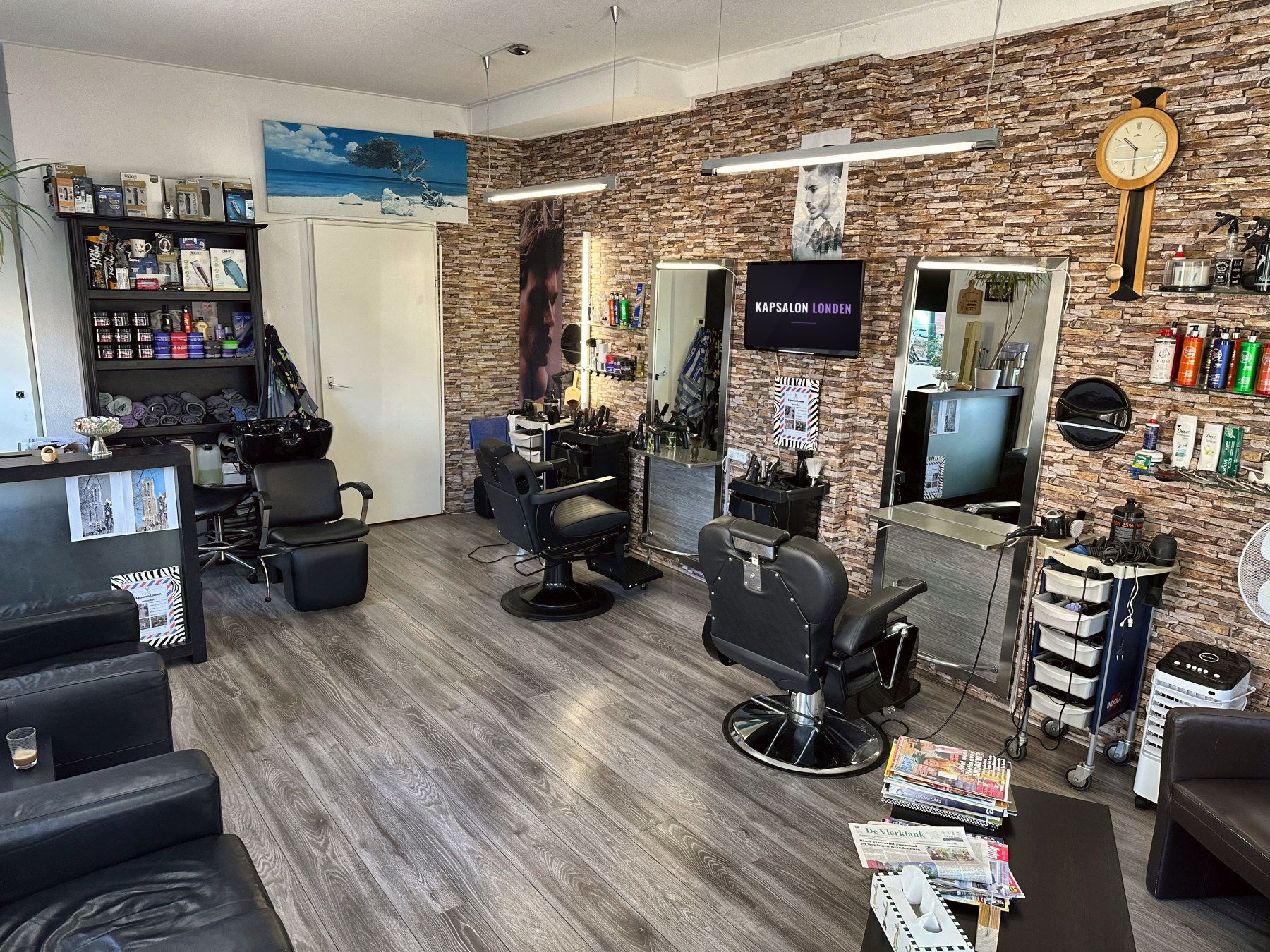 Het interieur van Kapsalon Londen met zwarte kappersstoelen, verlichte spiegels en een stenen muur