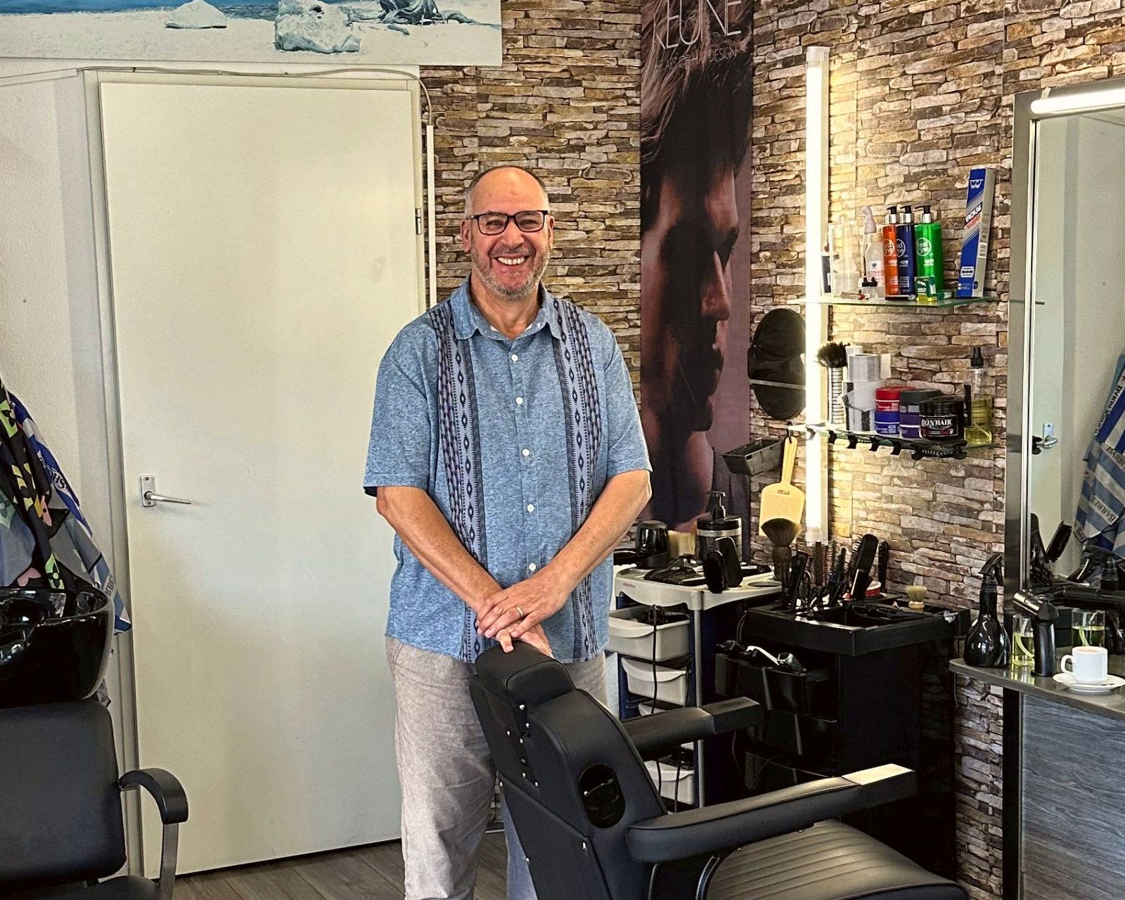 Nacer, eigenaar van Kapsalon Londen, lachend naast een kappersstoel in zijn zaak in De Bilt